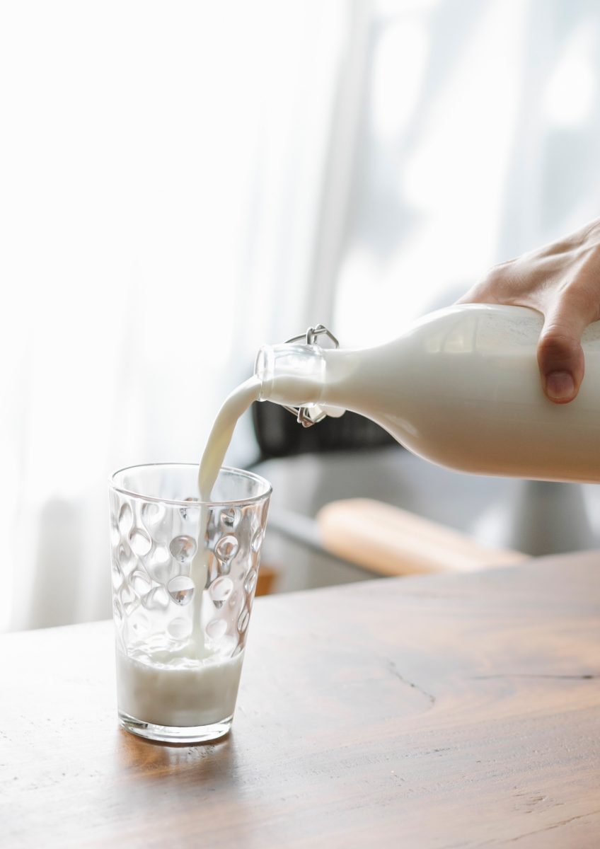 Hand pouring milk from a glass bottle into a glass