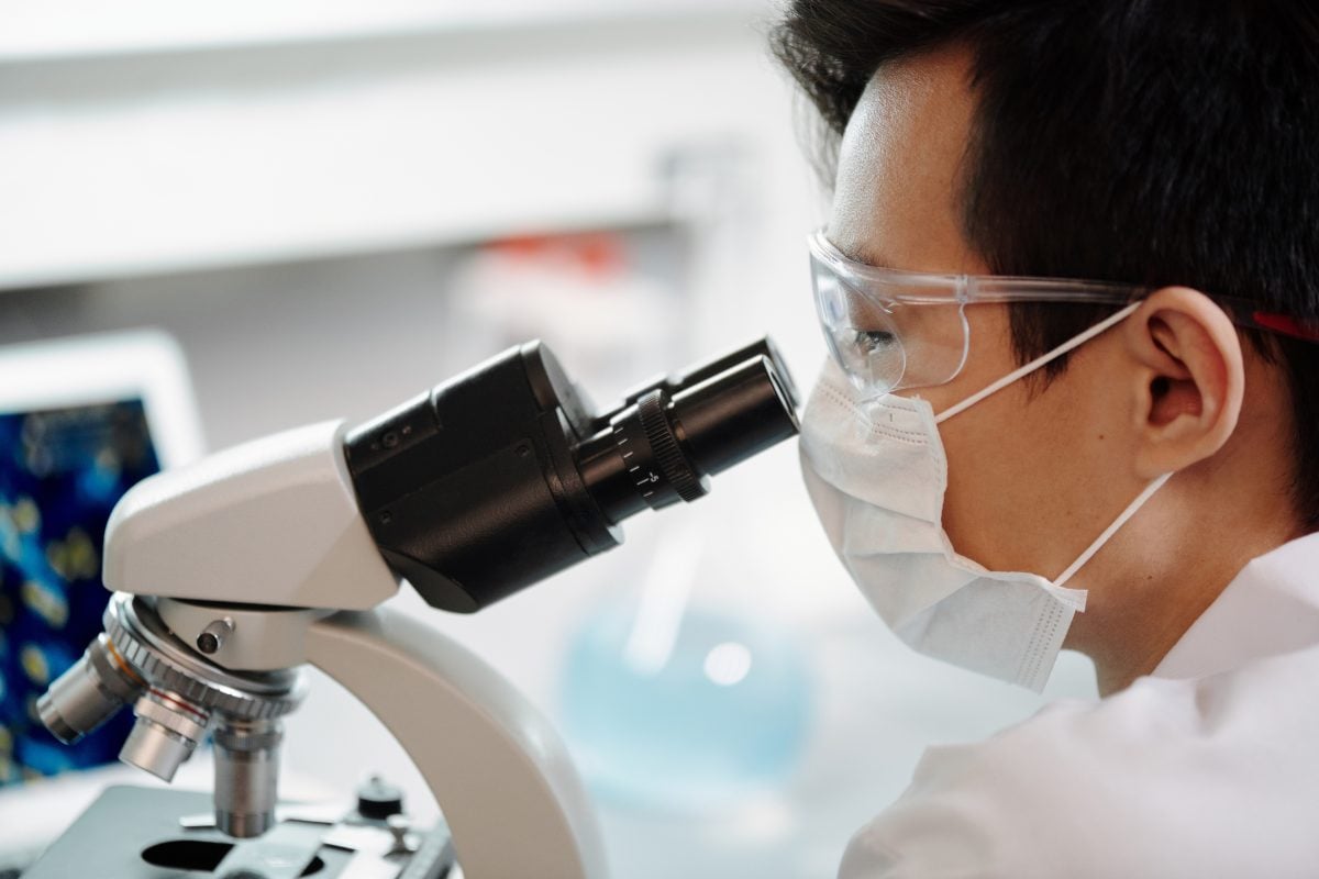 side profile of a man looking into a microscope in a lab wearing glasses and a lab coat