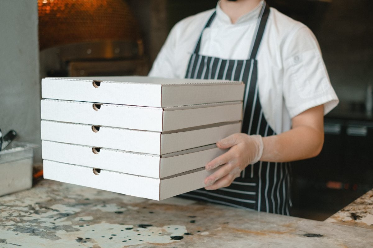 kitchen worker holding a stack of white pizza boxes