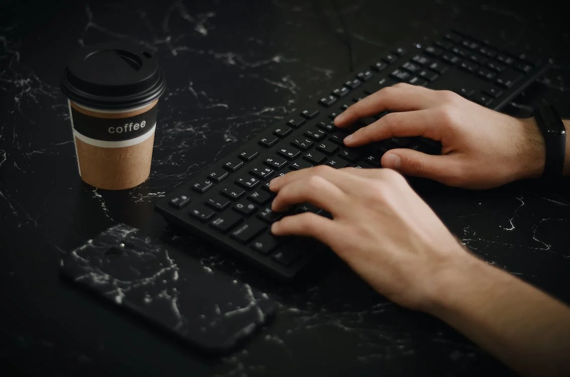 Hands typing on keyboard next to a cup of coffee