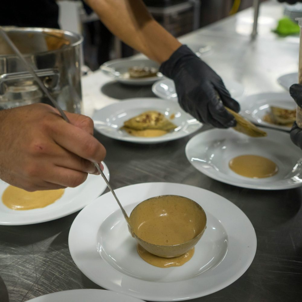 Close up shot of chefs preparing multiple dishes with sauce