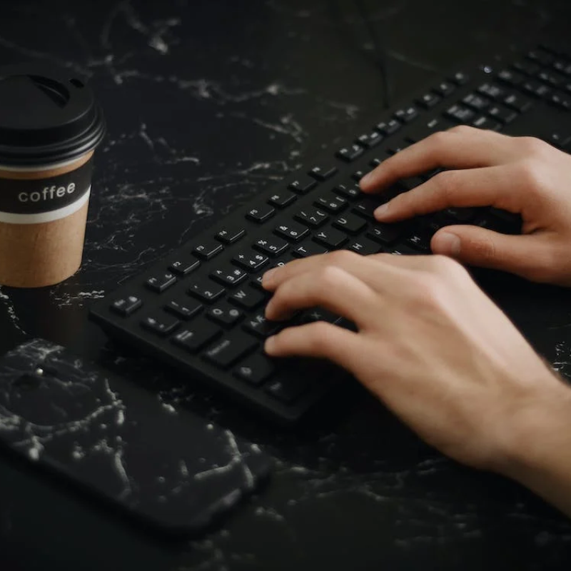 unnamed Hands typing on keyboard next to a cup of coffee